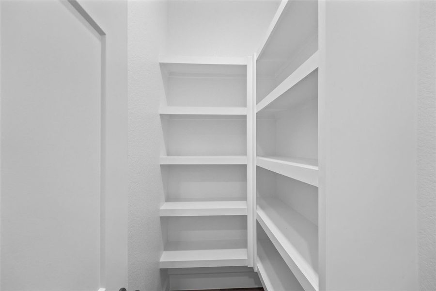 Spacious walk-in pantry offers exceptional storage potential, featuring multiple tiers of sturdy, built-in white shelving. Designed for maximum organization, the deep shelves provide ample space for all your culinary needs.