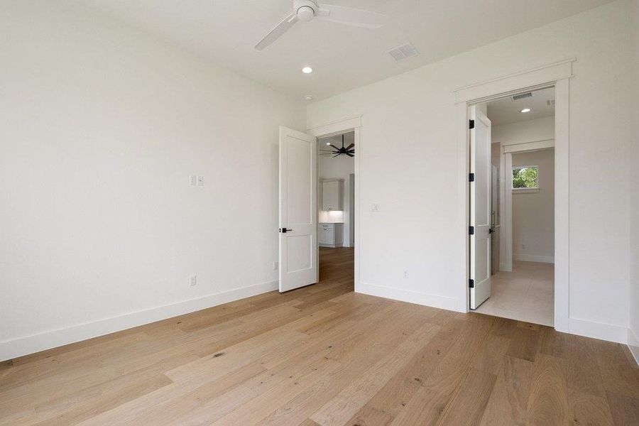 This room features light-toned hardwood flooring, white walls, and a ceiling fan