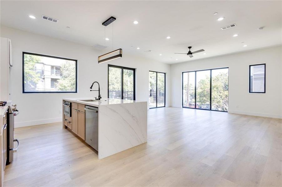 Kitchen with sink, hanging light fixtures, light stone counters, stainless steel appliances, and light wood-type flooring