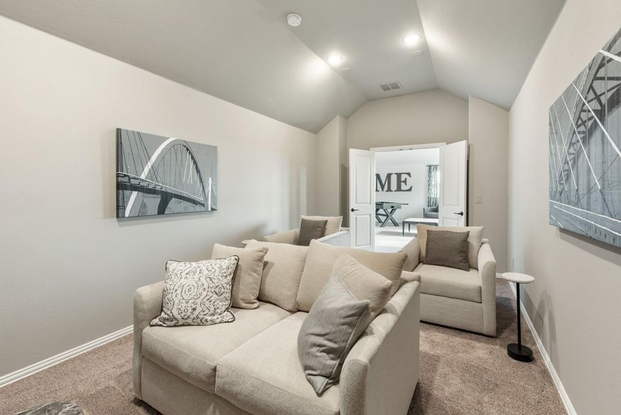 Sitting room with vaulted ceiling, beige sofa, accent chair, and carpet flooring