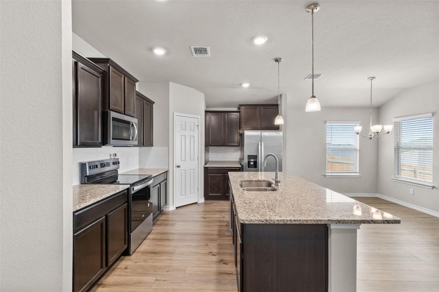 Kitchen with stainless steel appliances, dark wood finish cabinetry, decorative backsplash, light stone counters, and vaulted ceiling