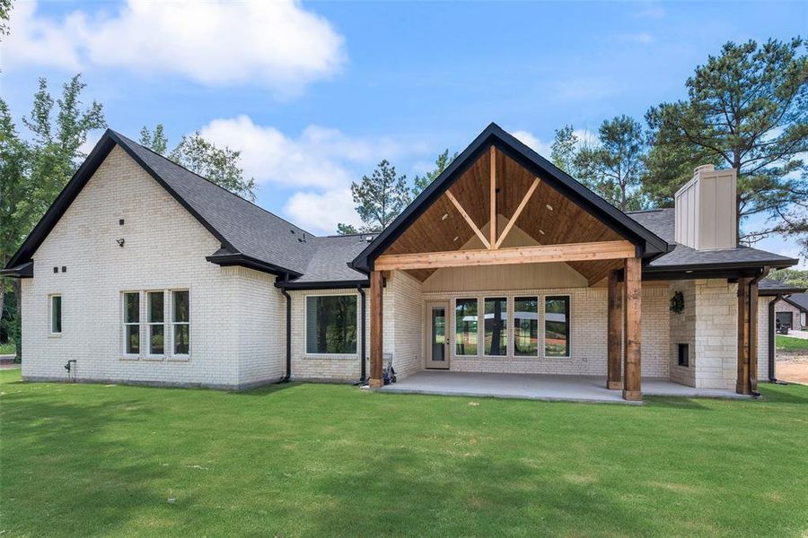 Expansive backyard featuring a manicured lawn, a covered patio with exposed wood beams, and a stone-clad outdoor fireplace