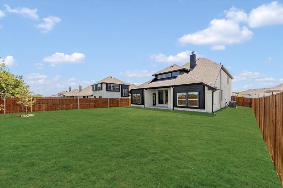 Backyard of two-story home with large green lawn, wood privacy fence, and dark siding exterior.