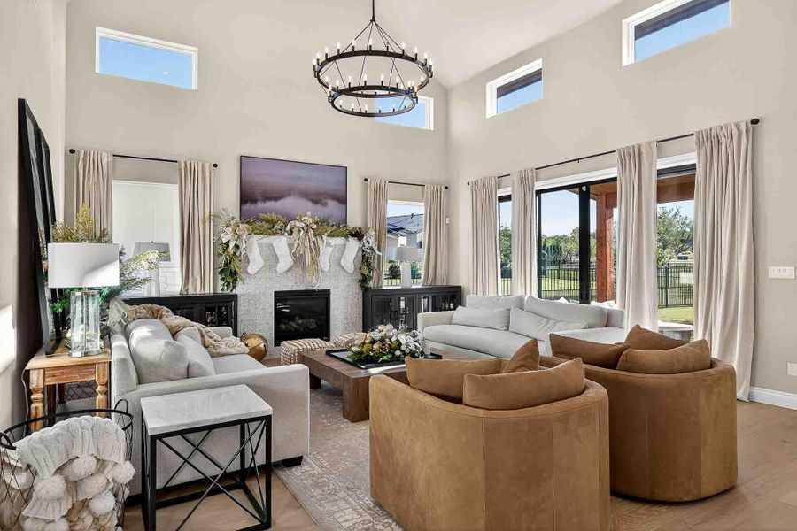 Living room with a high ceiling, a glass covered fireplace, healthy amount of natural light, wood finished floors, and a chandelier
