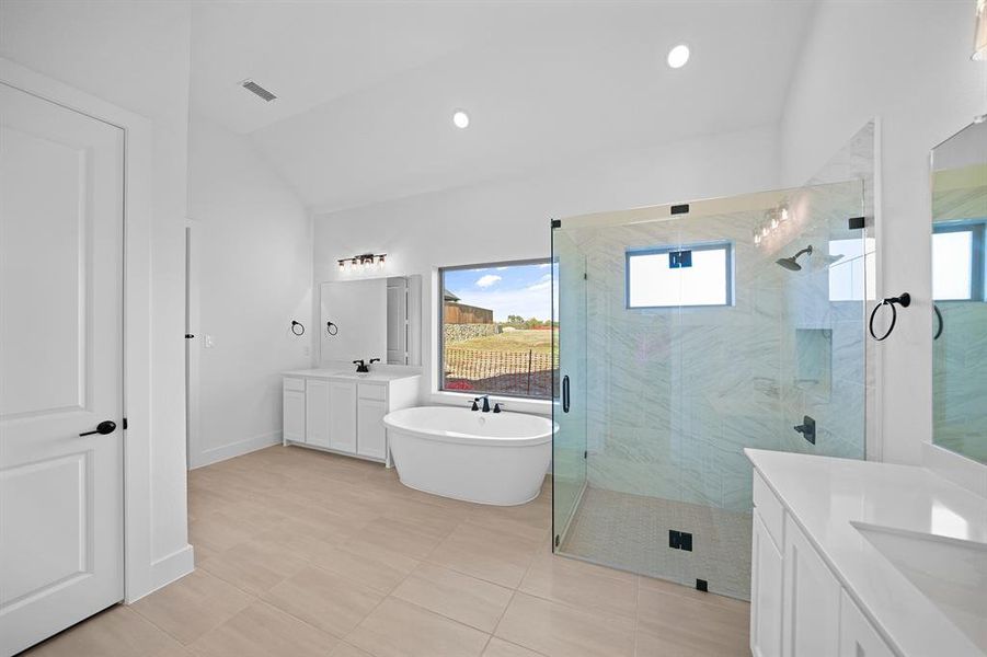 Bathroom with a freestanding tub, two vanities, a marble finish shower, lofted ceiling, and recessed lighting