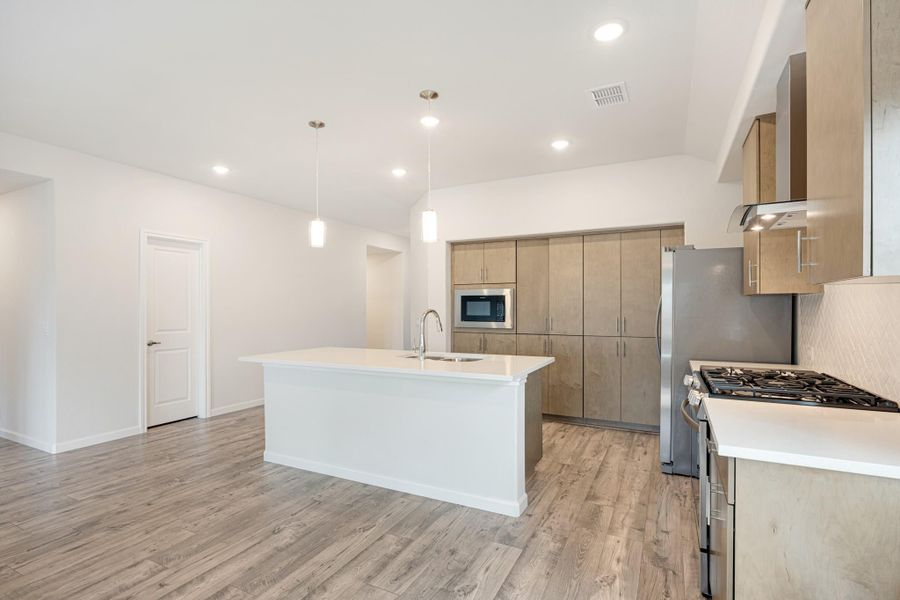Open kitchen with white island, light wood cabinets, stainless steel appliances, and hardwood floors