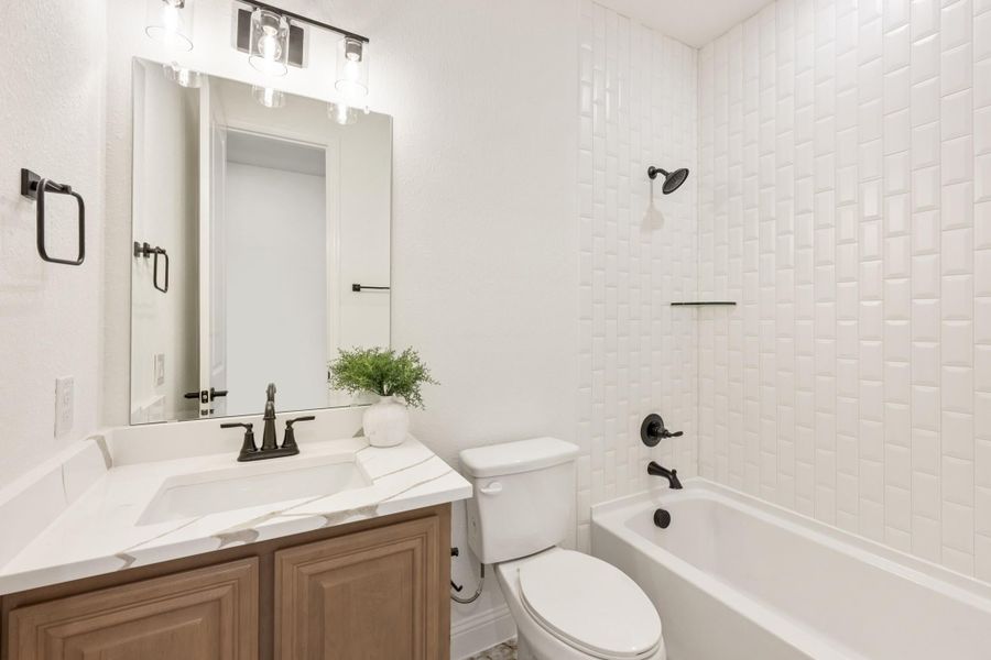 Bathroom with wood vanity, white quartz countertop, and tub-shower with white subway tile walls