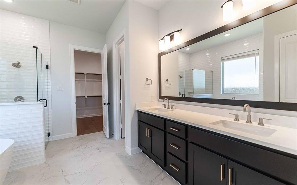 Spacious bathroom featuring a double vanity with dark cabinetry and light countertops, a large framed mirror, and a glass-enclosed shower with white subway tile Spacious bathroom featuring a double vanity with dark cabinetry and light countertops, a large framed mirror, and a glass-enclosed shower with white subway tile