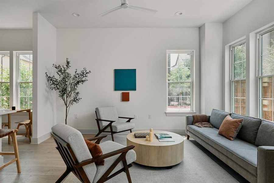 Open-concept living space featuring light wood-finish flooring, multiple large windows, recessed lighting, and a ceiling fan