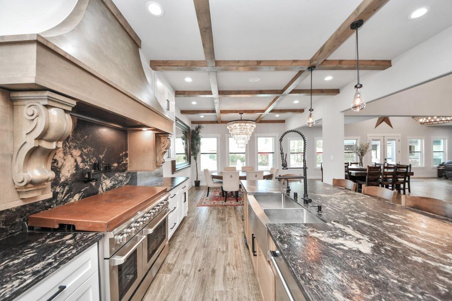 Stunning kitchen featuring a large marble island, elegant wood beam ceiling, and high-end stainless steel appliances, seamlessly flowing into an open dining area with abundant natural light.