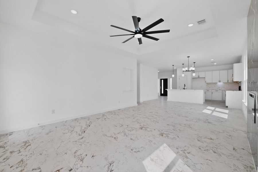Unfurnished living room featuring a tray ceiling, ceiling fan, light, and suspended lighting