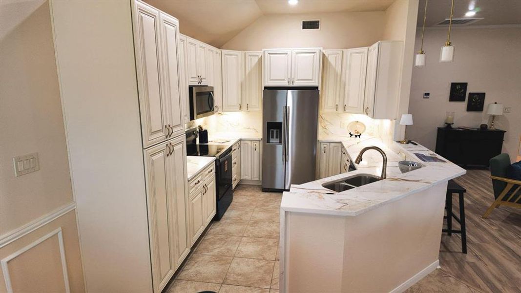 Kitchen featuring shaker-style cabinetry, stainless steel appliances, a double basin sink, tile flooring, and a peninsula with a breakfast bar