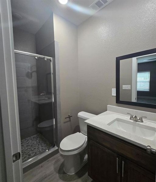 Bathroom featuring a glass-enclosed shower with pebble-style flooring, a wood-finish vanity with a white countertop and integrated sink, and brushed nickel fixtures