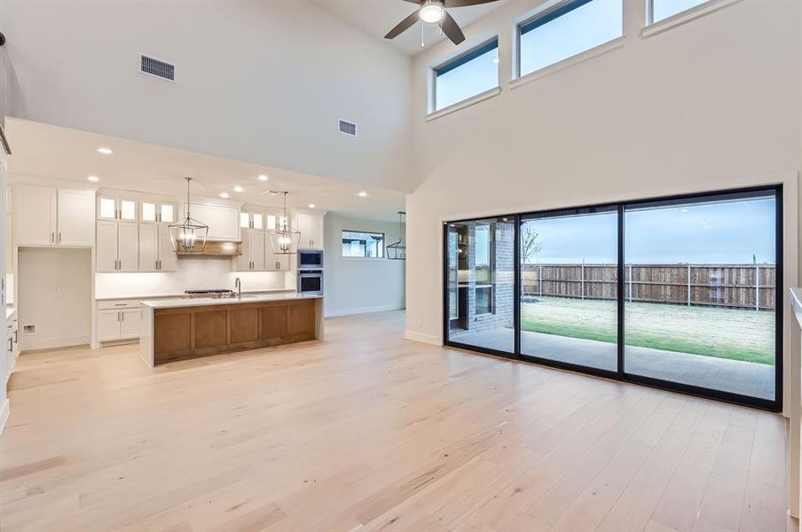 Unfurnished living room with ceiling fan with notable chandelier, light wood-type flooring, and a high ceiling