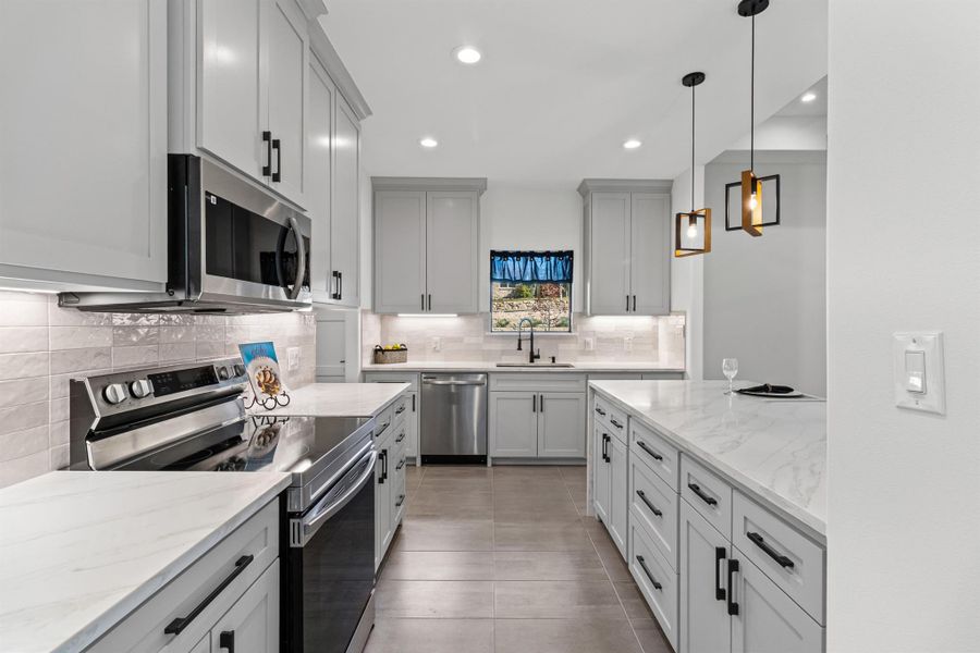Kitchen with appliances with stainless steel finishes, light stone countertops, pendant lighting, backsplash, and recessed lighting