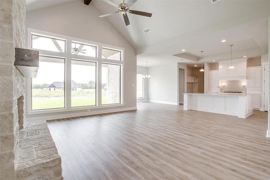 Unfurnished living room featuring high vaulted ceiling, ceiling fan with notable chandelier, light hardwood / wood-style floors, and a stone fireplace