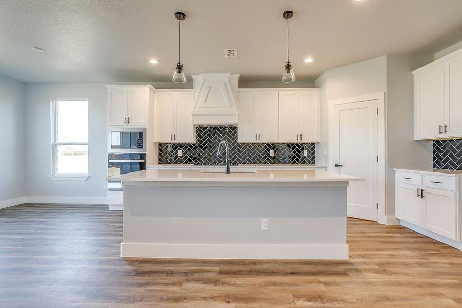 Kitchen with decorative backsplash, white cabinetry, stainless steel appliances, light wood-style floors, and light stone counters