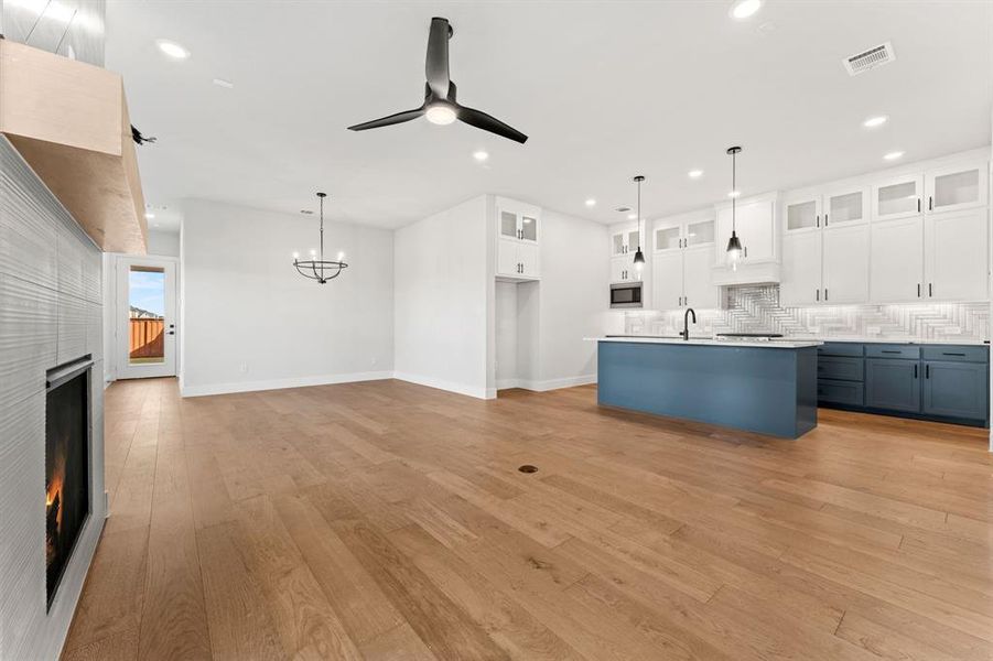 Kitchen with tasteful backsplash, white cabinetry, pendant lighting, and ceiling fan with notable chandelier