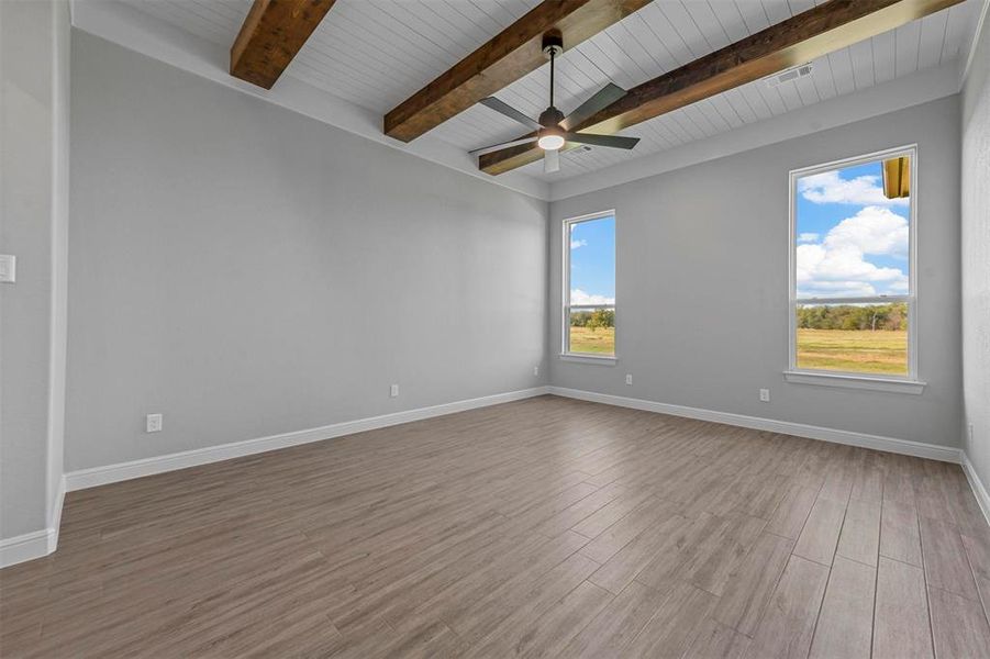 Spare room featuring a wealth of natural light, light hardwood / wood-style flooring, beamed ceiling, and ceiling fan