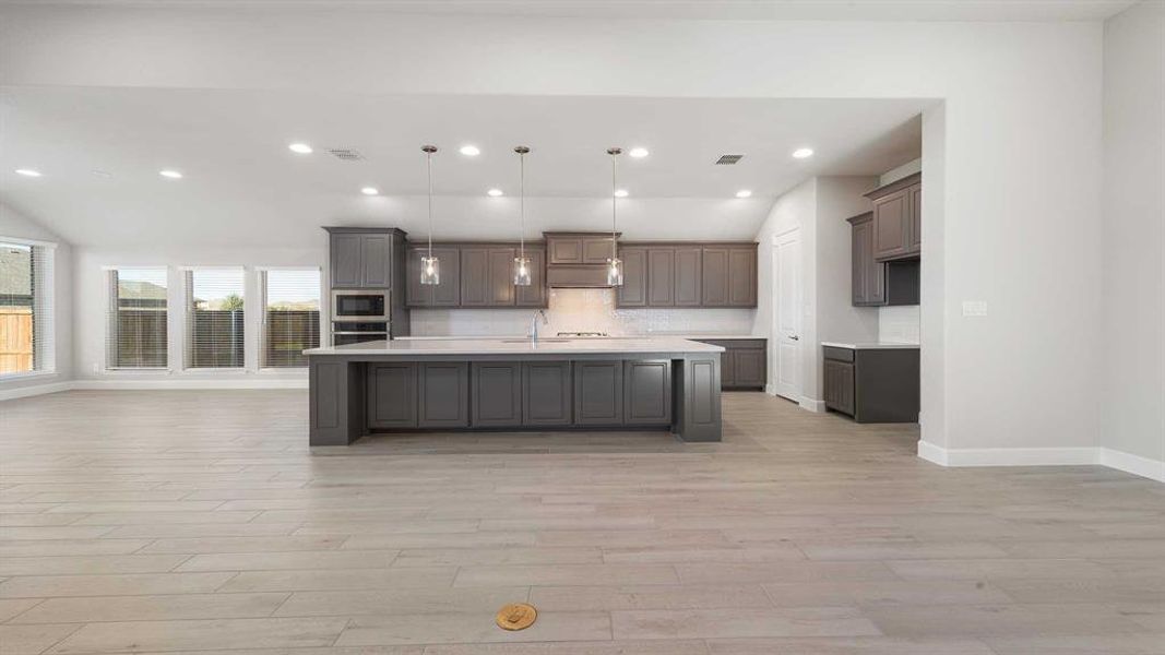 Kitchen with stainless steel appliances, hanging light fixtures, lofted ceiling, a center island with sink, and light wood-type flooring