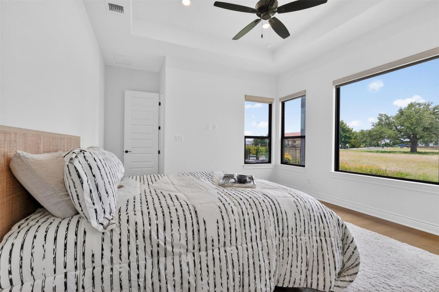 Natural light floods this spacious primary bedroom, featuring a tray ceiling and a sweeping view of the open landscape. Natural light floods this spacious primary bedroom, featuring a tray ceiling and a sweeping view of the open landscape.