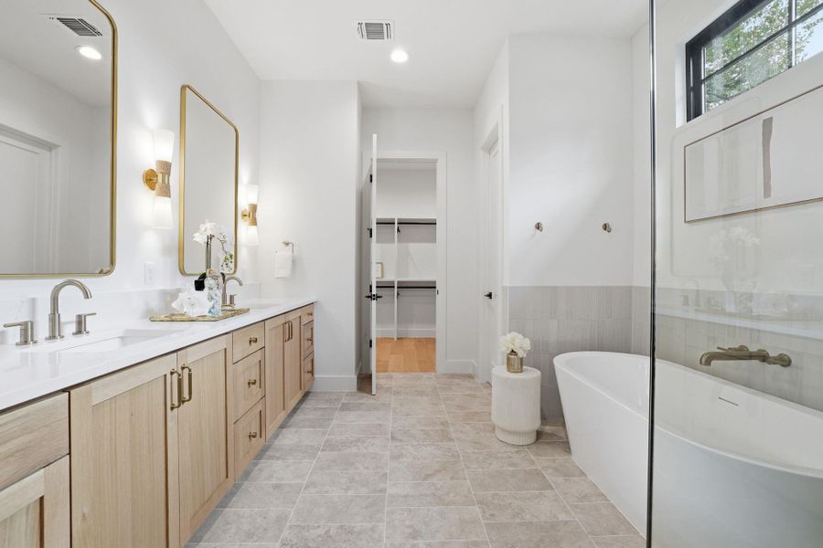 Full bathroom with a walk in closet, a soaking tub, double vanity, light tile patterned floors, and tile walls