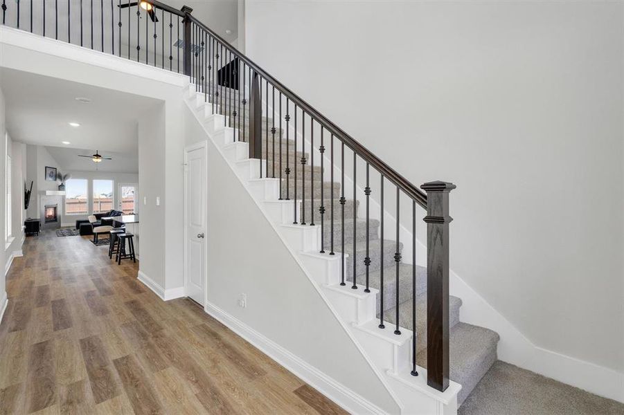 Entryway featuring wood-finish flooring, a carpeted staircase with dark wood newel posts and wrought iron balusters, and an upper-level landing with matching balusters
