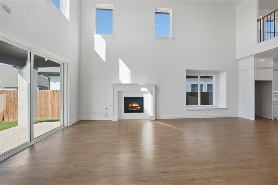 Unfurnished living room featuring a lit fireplace, a towering ceiling, and wood finished floors Unfurnished living room featuring a lit fireplace, a towering ceiling, and wood finished floors
