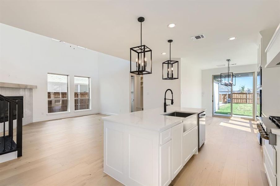 Kitchen featuring white cabinets, an island with sink, stainless steel dishwasher, light hardwood / wood-style flooring, and pendant lighting