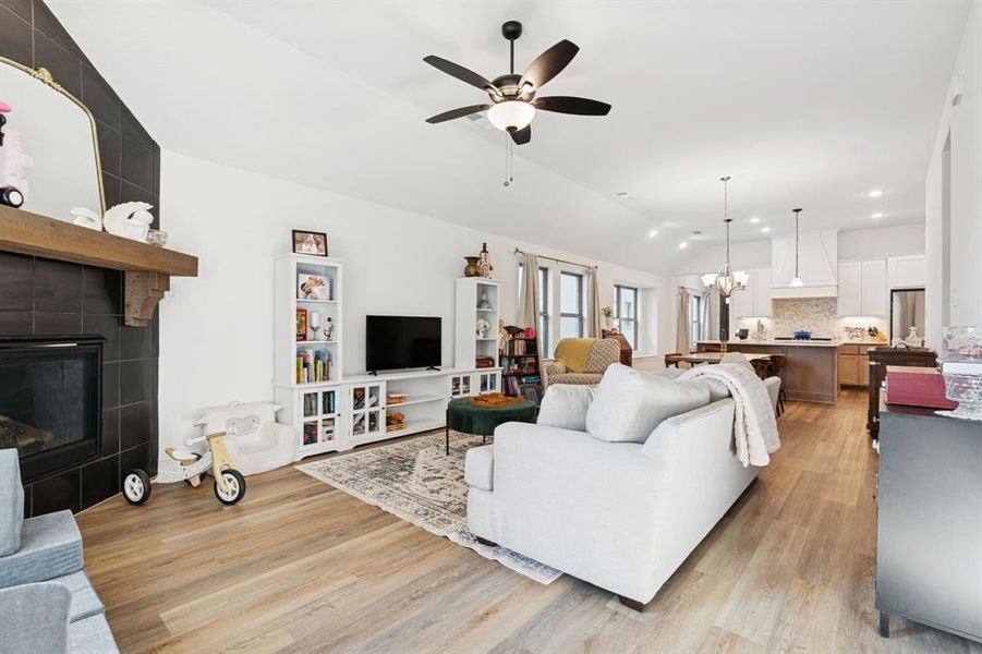 Living room featuring a tiled fireplace, lofted ceiling, a chandelier, light wood-style floors, and ceiling fan Living room featuring a tiled fireplace, lofted ceiling, a chandelier, light wood-style floors, and ceiling fan