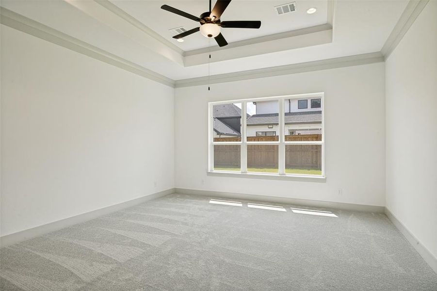 Spacious interior room featuring light gray carpeting, neutral wall tones, and a tray ceiling with a ceiling fan Spacious interior room featuring light gray carpeting, neutral wall tones, and a tray ceiling with a ceiling fan