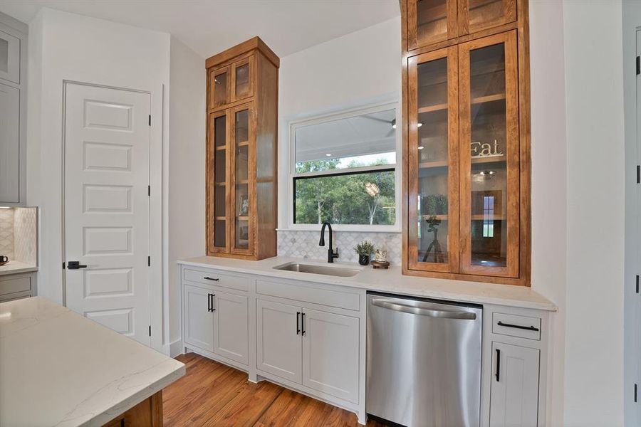 Bar area with stainless steel dishwasher, tasteful backsplash, light wood-type flooring, and light stone counters Bar area with stainless steel dishwasher, tasteful backsplash, light wood-type flooring, and light stone counters