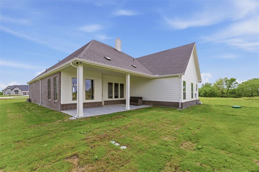 Expansive backyard featuring a covered patio with concrete flooring, support columns, and a shingle roof