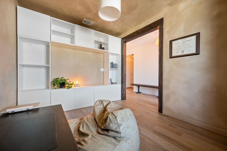 Office area featuring light wood finished floors, built in features, and a textured wall Office area featuring light wood finished floors, built in features, and a textured wall