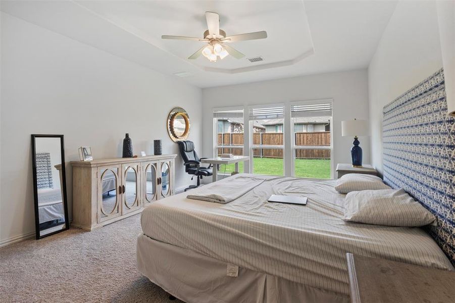 Carpeted bedroom with a tray ceiling and a ceiling fan