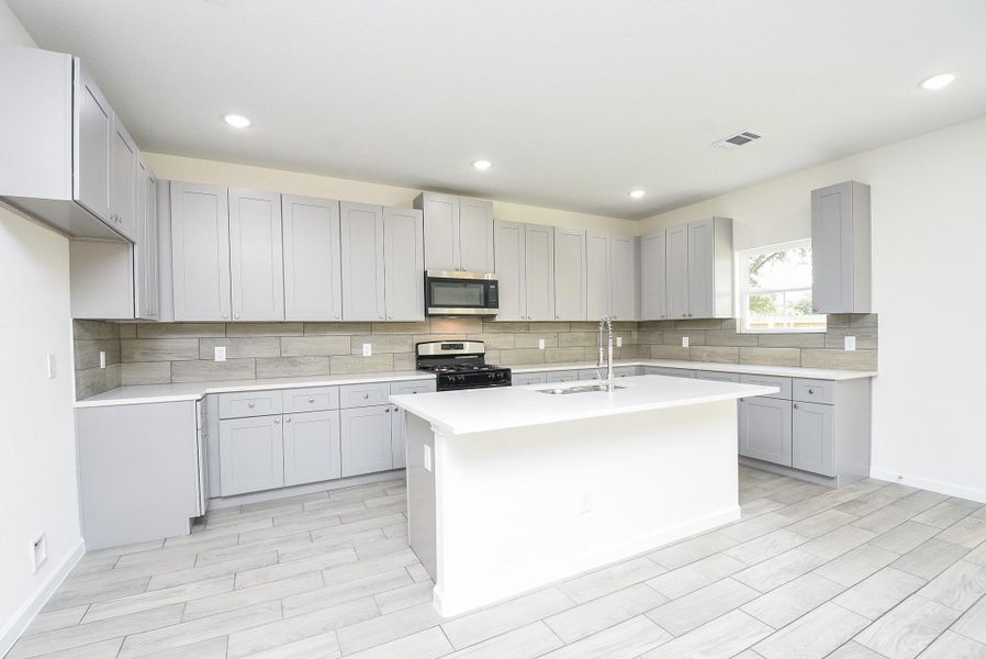 Modern kitchen featuring gray shaker cabinets, stainless steel appliances, herringbone tile backsplash, and a central island. Bright space with tiled flooring and recessed lighting. Modern kitchen featuring gray shaker cabinets, stainless steel appliances, herringbone tile backsplash, and a central island. Bright space with tiled flooring and recessed lighting.