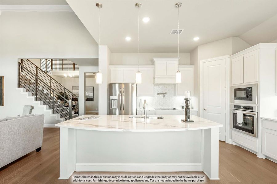 Open kitchen with large white island, white cabinets, stainless appliances, and pendant lights over hardwood floors