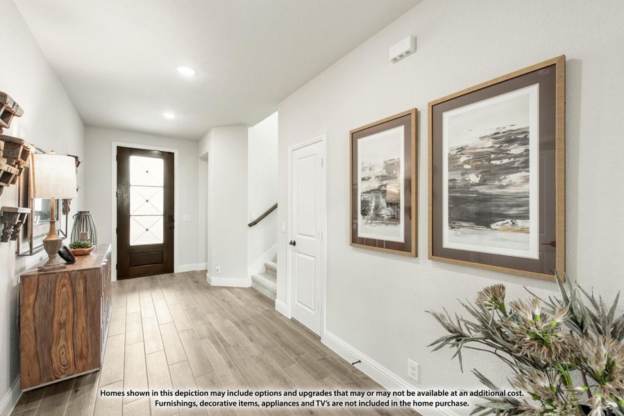Home entryway with dark wood front door, light hardwood floors, staircase, and two framed wall art pieces