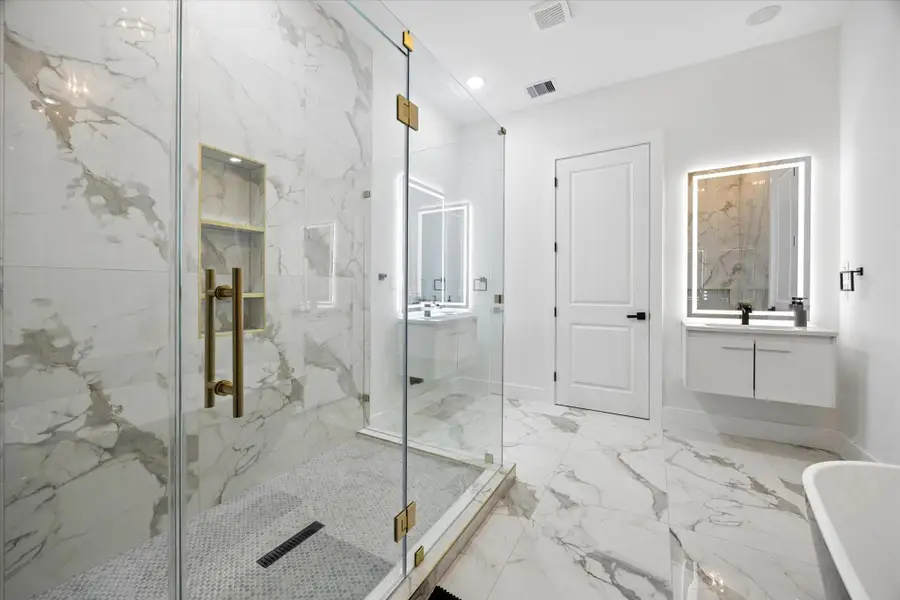 This bathroom features elegant marble tiles, a spacious glass-enclosed shower with gold fixtures, a modern floating vanity with an illuminated mirror, and a sleek standalone bathtub, creating a luxurious and contemporary space. This bathroom features elegant marble tiles, a spacious glass-enclosed shower with gold fixtures, a modern floating vanity with an illuminated mirror, and a sleek standalone bathtub, creating a luxurious and contemporary space.