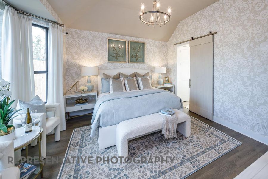 Bedroom featuring wallpapered walls, vaulted ceiling, a barn door, wood finished floors, and a chandelier Bedroom featuring wallpapered walls, vaulted ceiling, a barn door, wood finished floors, and a chandelier