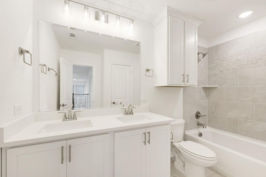 Bathroom with double sink vanity, white cabinets, large mirror, and tiled tub-shower combo