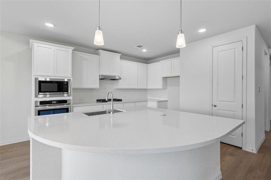 Kitchen with white cabinets, light wood-type flooring, hanging light fixtures, and recessed lighting Kitchen with white cabinets, light wood-type flooring, hanging light fixtures, and recessed lighting