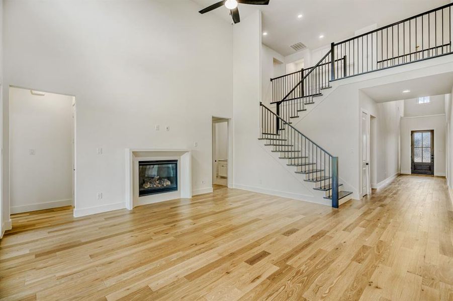 Unfurnished living room featuring a glass covered fireplace, light wood-style floors, a ceiling fan, a high ceiling, and recessed lighting