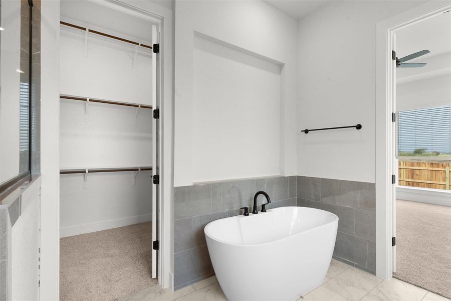 Bathroom with a freestanding bath, tile walls, light colored carpet, wainscoting, and a ceiling fan