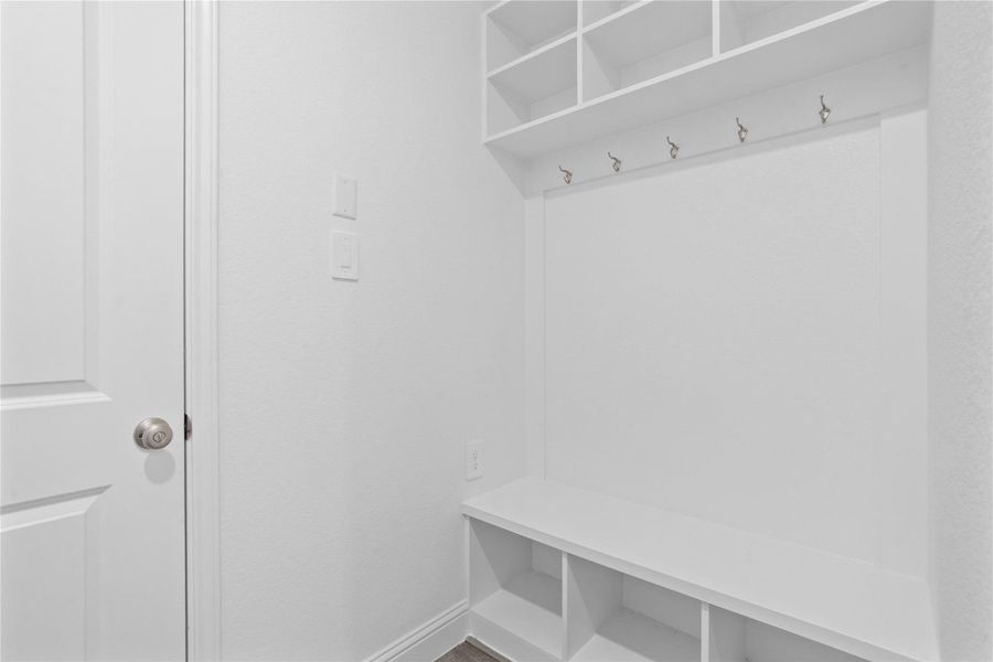 Step into this highly functional and stylish mudroom drop zone, an essential feature for a busy household. The space boasts custom-built white cabinetry and shelving, providing generous storage for coats, bags, and shoes. A comfortable built-in bench offers a convenient spot to sit, while three sleek hooks keep outerwear tidy and accessible.