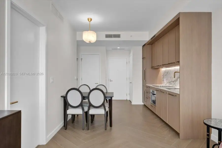 Kitchen featuring light wood-finish cabinetry, integrated appliances, stone backsplash, and herringbone-pattern wood-finish flooring, accented by a modern brass pendant fixture