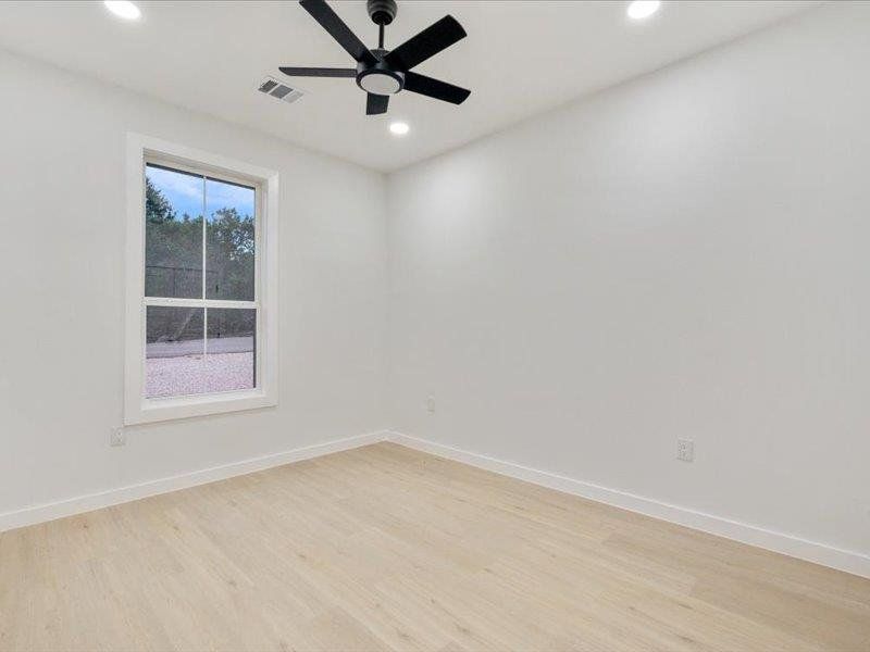 This room features light-colored flooring, a window with white trim, and a black ceiling fan
