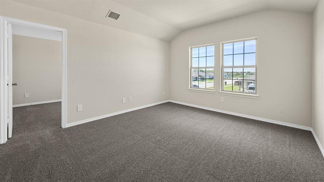 Spacious interior room with neutral-toned walls, vaulted ceiling, and grey carpet flooring