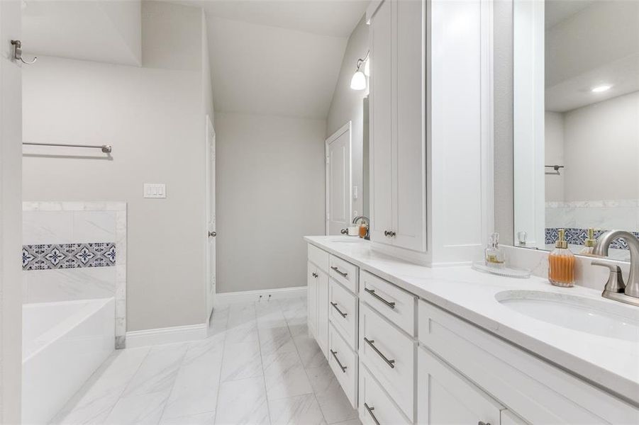 Full bathroom with double vanity, a bath, light marble finish floors, and lofted ceiling Full bathroom with double vanity, a bath, light marble finish floors, and lofted ceiling