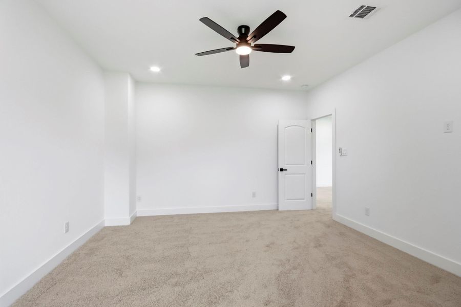Spacious bedroom with plush carpeting, recessed lighting, and a modern ceiling fan, offering a comfortable and inviting atmosphere.